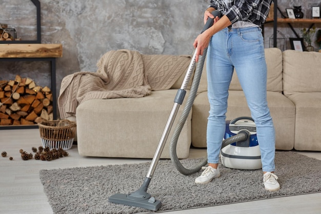 Imagen recortada de hermosa mujer joven con una aspiradora mientras limpia la alfombra en la casa