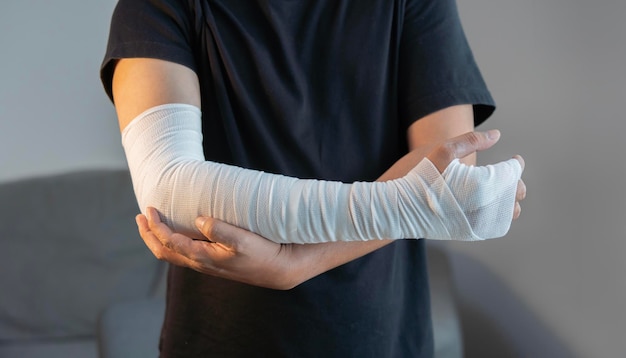 Imagen recortada de un hombre adulto con una venda de gasa envuelta alrededor de su brazo herido en casa