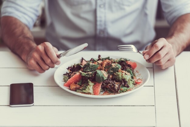 Imagen recortada de hombre comiendo ensalada en café.