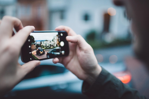 Imagen recortada de un hombre fotografiando un coche a través de un teléfono móvil
