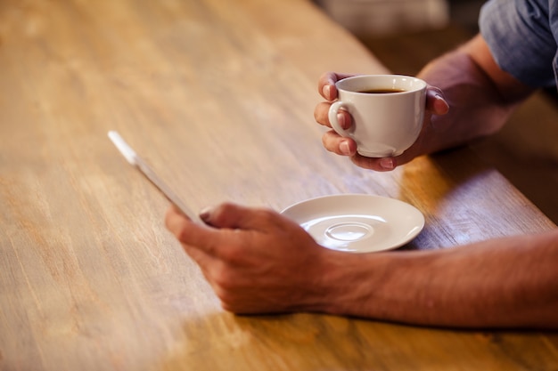 Imagen recortada del hombre hipster con teléfono inteligente mientras bebe una taza de café