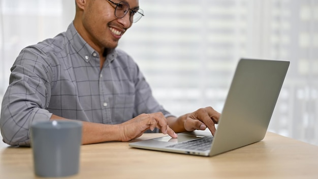 Imagen recortada de un hombre de negocios asiático profesional usando su computadora portátil en su escritorio