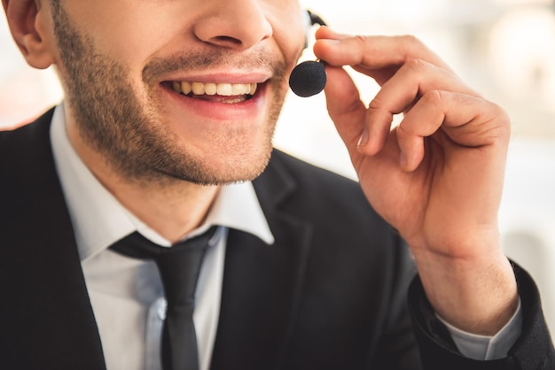 Imagen recortada de un hombre de negocios atractivo con traje y auriculares hablando y sonriendo mientras trabaja en la oficina