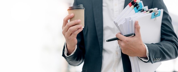 Imagen recortada de un hombre de negocios con traje sosteniendo un montón de documentos y una taza de café de pie en el espacio de copia de fondo blanco