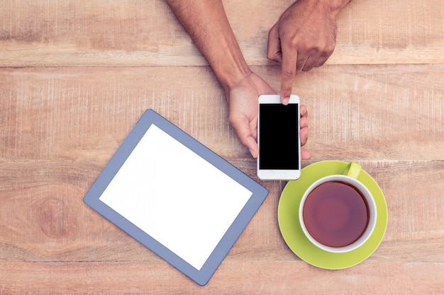 Imagen recortada del hombre que usa el teléfono inteligente por el café y la tableta en la mesa