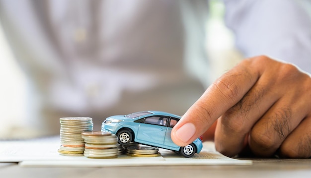 Imagen recortada de un hombre sosteniendo un coche de juguete con monedas en la mesa