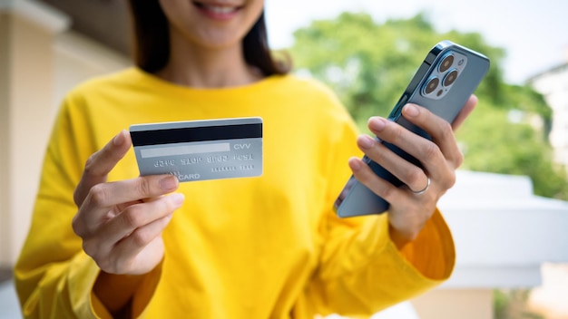 Imagen recortada de una joven feliz que tiene una factura de pago con tarjeta de crédito con pago en línea a través de Internet en un teléfono inteligente