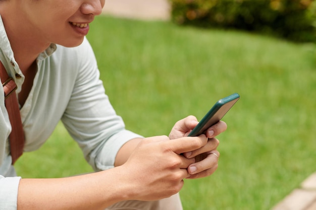 Imagen recortada de un joven sonriente enviando mensajes de texto a su amiga o novia