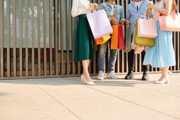 Imagen recortada de jóvenes con muchas bolsas de la compra de pie al aire libre y discutiendo compras