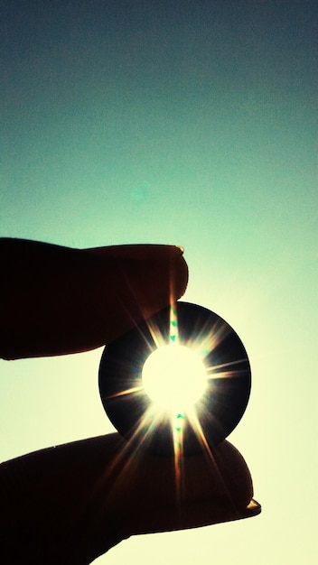 Foto imagen recortada de una lente en la mano contra el sol brillante