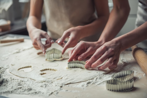 Imagen recortada de mamá e hija en delantales usando cortadores de masa de diferentes formas para hacer galletas