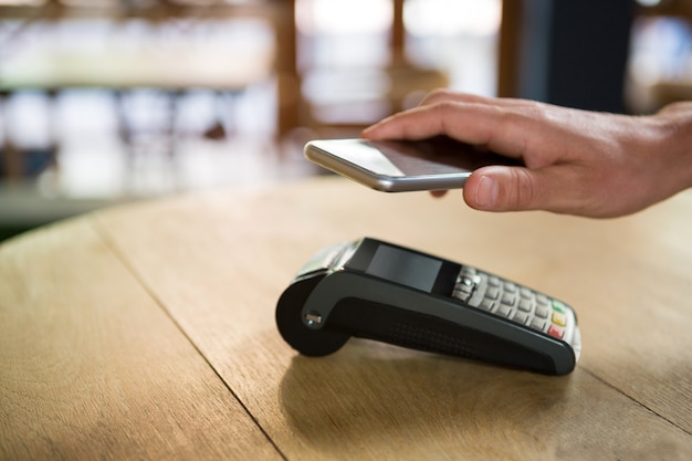 Imagen recortada de la mano del cliente pagando a través de teléfonos inteligentes en la cafetería.