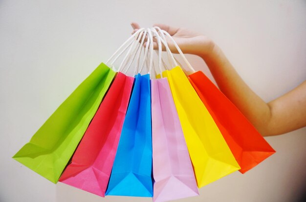 Imagen recortada de la mano llevando bolsas de compras de varios colores contra un fondo gris