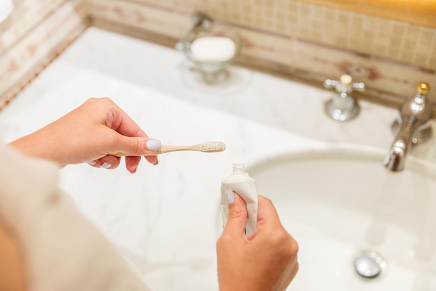 Imagen recortada de la mano de una mujer atractiva aplicando pasta de dientes en el cepillo de dientes en el baño Concepto de mañana de belleza saludable y bienestar