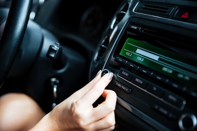 Foto imagen recortada de una mano de mujer girando el botón de la radio en el coche