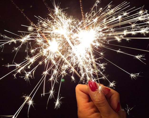 Foto imagen recortada de la mano de una mujer sosteniendo una chispa por la noche