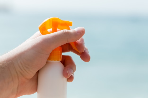 Imagen recortada de la mano de la mujer sosteniendo spray protector solar en el fondo del mar.