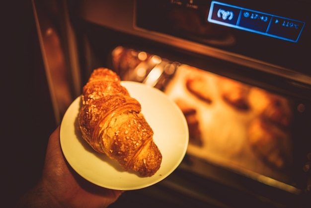 Foto imagen recortada de la mano poniendo un croissant en el horno