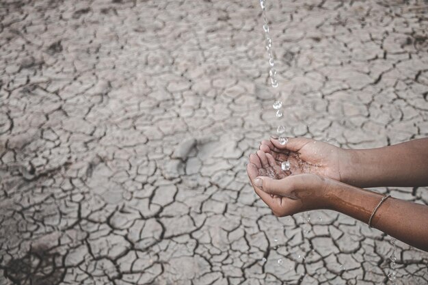 Foto imagen recortada de una mano sosteniendo agua contra una tierra estéril