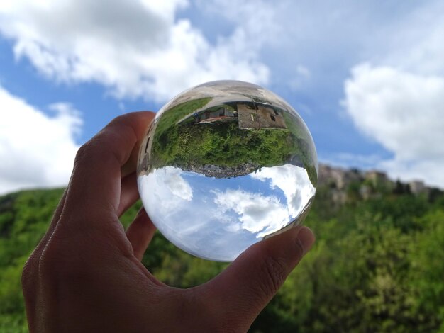 Foto imagen recortada de una mano sosteniendo una bola de cristal contra el cielo