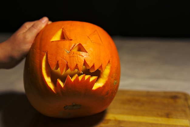 Foto imagen recortada de una mano sosteniendo una calabaza de halloween en la mesa