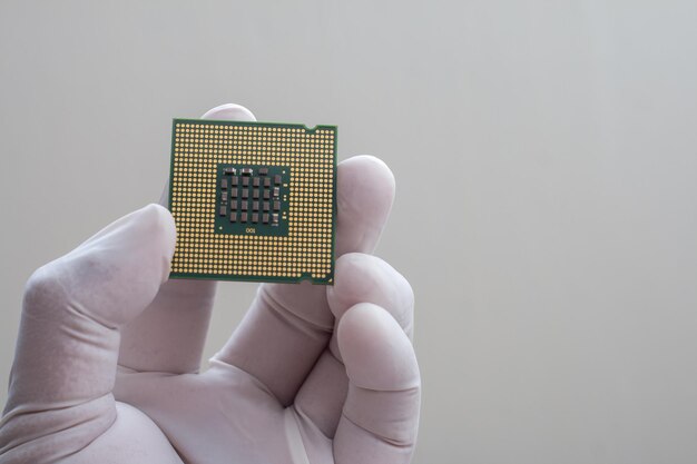 Imagen recortada de una mano sosteniendo un chip de computadora contra un fondo gris