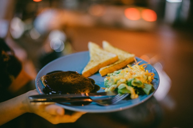 Foto imagen recortada de una mano sosteniendo comida en un plato durante la noche al aire libre