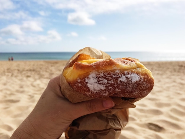 Foto imagen recortada de una mano sosteniendo comida en la playa contra el cielo