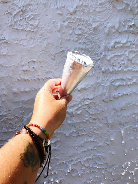 Foto imagen recortada de la mano sosteniendo un cono de helado frente a la pared