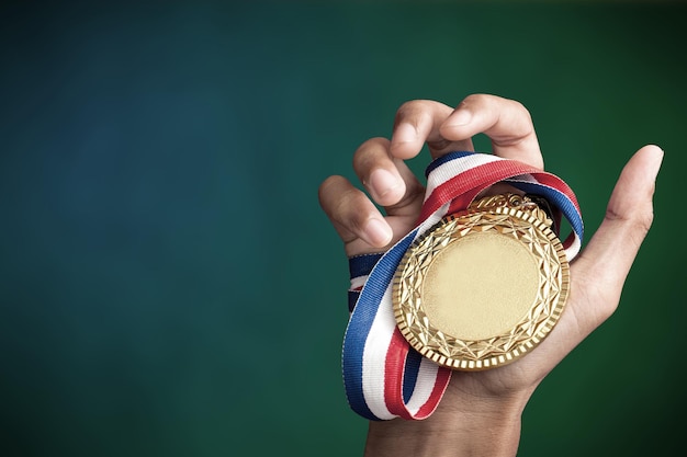 Foto imagen recortada de una mano sosteniendo una medalla de oro contra un fondo de color