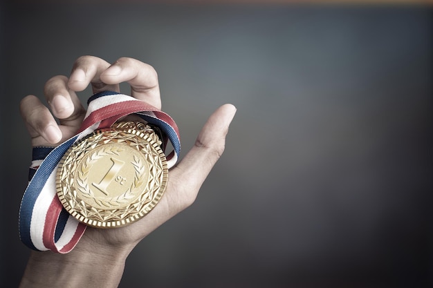 Imagen recortada de una mano sosteniendo una medalla de oro contra un fondo de color