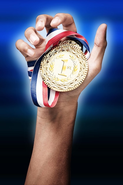 Imagen recortada de una mano sosteniendo una medalla de oro contra un fondo de color