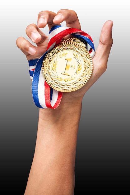 Imagen recortada de una mano sosteniendo una medalla de oro contra un fondo gris