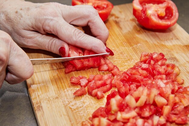 Imagen recortada de una mano sosteniendo pimientos rojos en la tabla de cortar