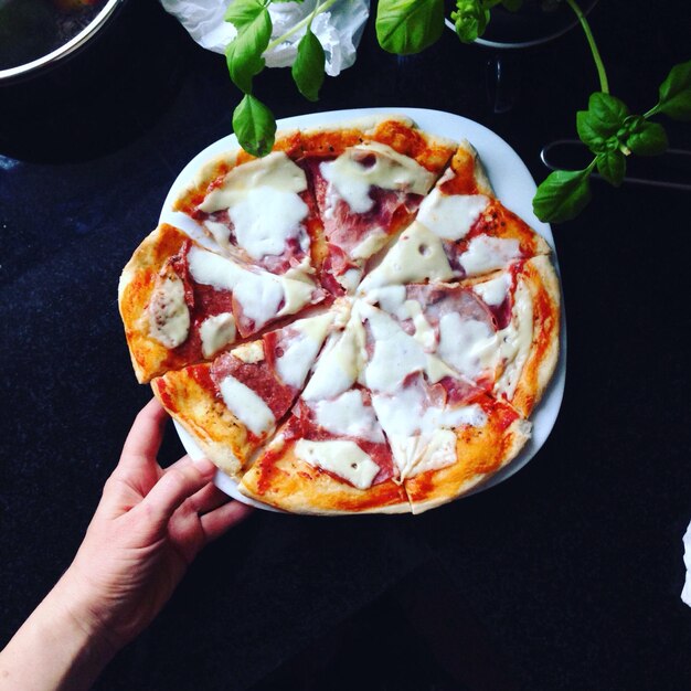 Foto imagen recortada de una mano sosteniendo un plato con pizza en la mesa