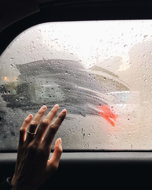 Imagen recortada de la mano tocando la ventana mojada del coche