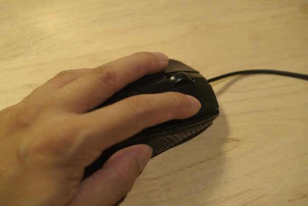 Imagen recortada de la mano usando el ratón de la computadora en la mesa