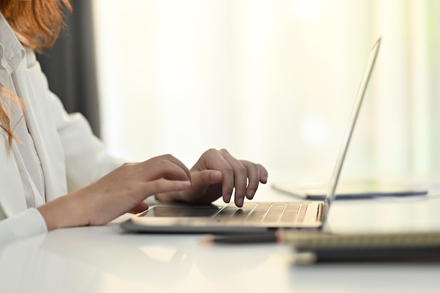 Imagen recortada de las manos de una empleada escribiendo en una computadora portátil trabajando en un escritorio de oficina blanco