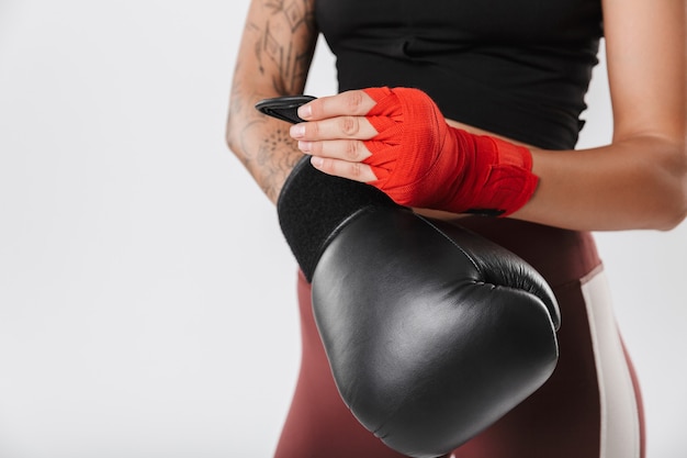 Imagen recortada de mujer activa con entrenamiento de ropa deportiva en guantes de boxeo y vendas de mano aisladas sobre pared blanca