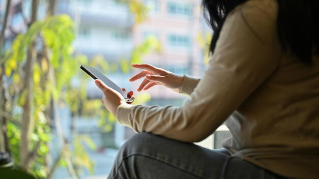 Imagen recortada de una mujer asiática con ropa informal usando su teléfono inteligente enfriándose en el café