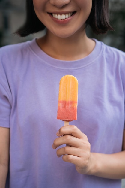 Imagen recortada de una mujer asiática sonriente con una camiseta morada con helado