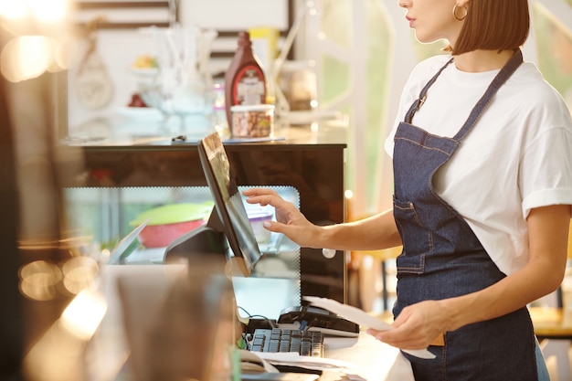 Foto imagen recortada de una mujer barista que trabaja en la cafetería y usa la caja registradora al aceptar el pago o ingresar detalles del pedido.