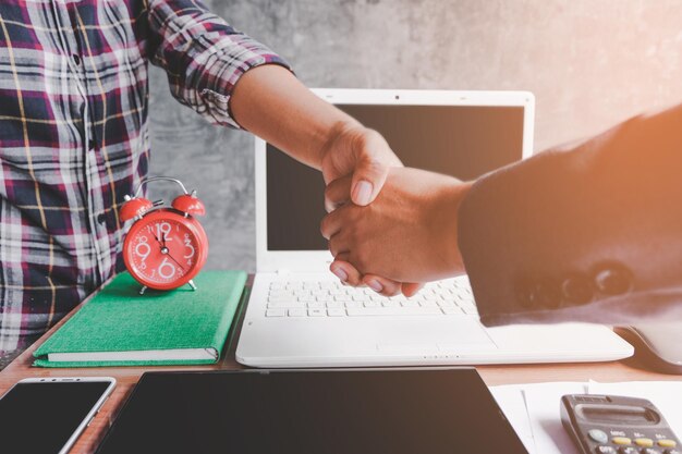 Imagen recortada de una mujer estrechando la mano de un colega mientras las tecnologías están en la mesa