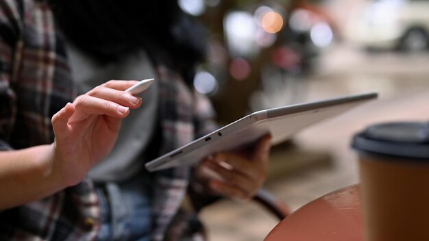 Foto imagen recortada de una mujer hipster asiática con camisa de franela usando una tableta mientras se relaja al aire libre