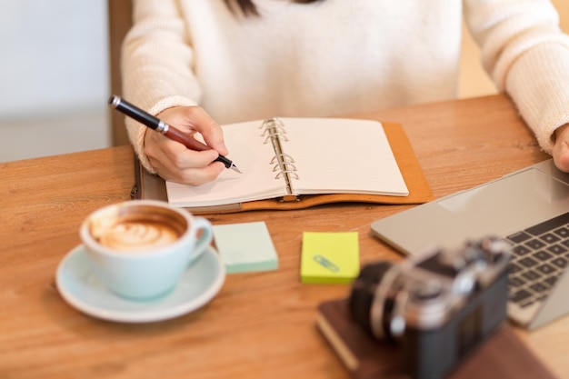 Imagen recortada de una mujer joven escribiendo sus rutinas diarias en su diario personal en el café