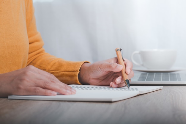 Imagen recortada de mujer de negocios sentada en la mesa y tomando notas en el cuaderno