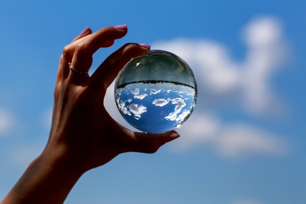 Foto imagen recortada de una mujer sosteniendo una bola de cristal contra el cielo azul