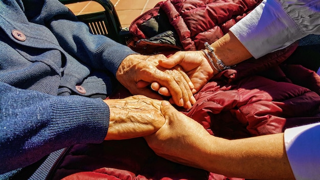 Foto imagen recortada de una mujer sosteniendo las manos de una persona mayor