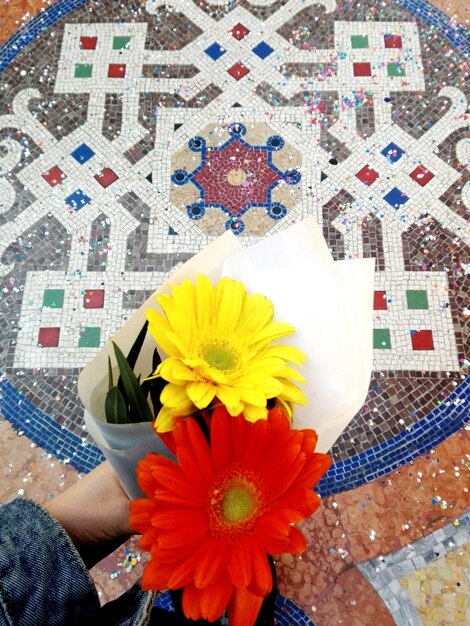 Imagen recortada de una mujer sosteniendo un ramo de flores sobre un piso de baldosas