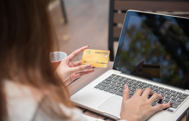 Imagen recortada de una mujer sosteniendo una tarjeta de crédito con una computadora portátil en la mesa
